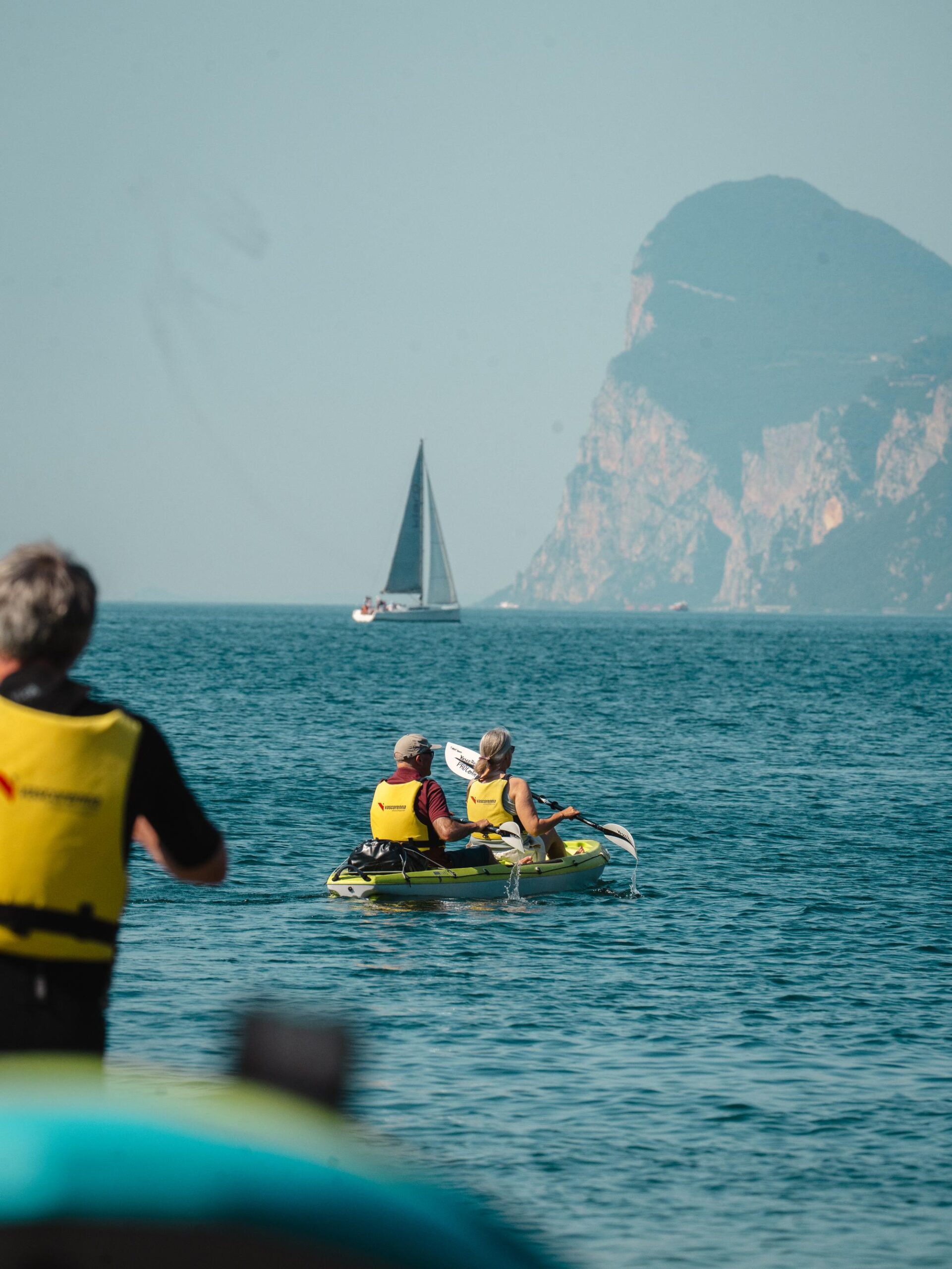 Persone in kayak sul Lago di Garda a Torbole, con una barca a vela e la falesia sullo sfondo